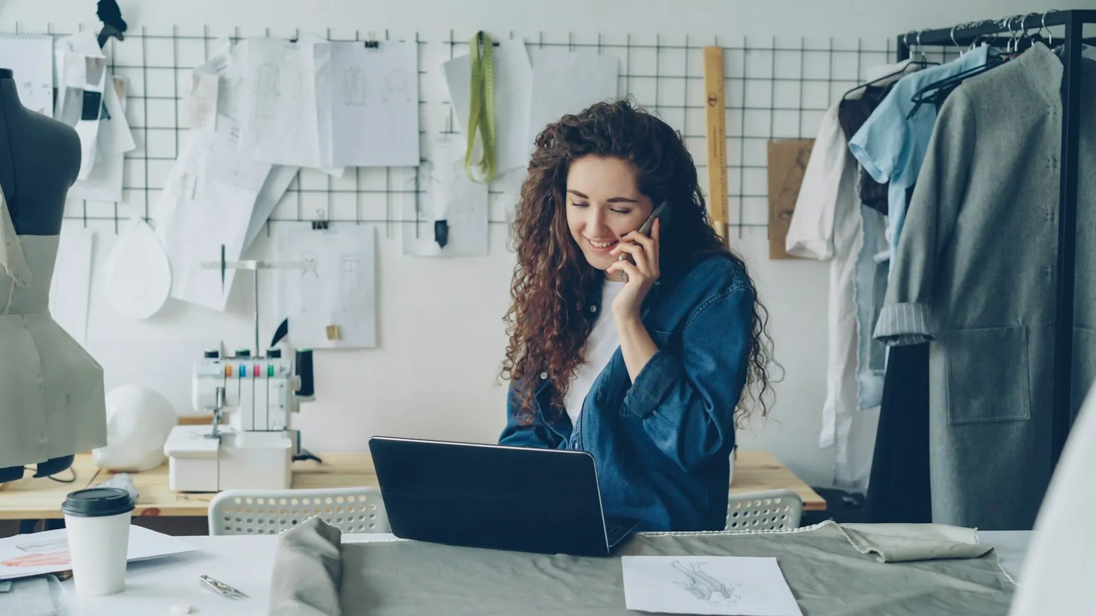 Designer de moda ao telefone, trabalhando em um laptop
