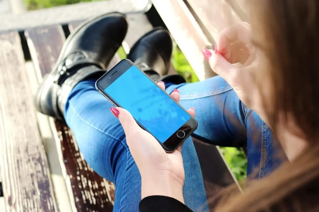 Dona de loja de cosméticos compara no celular a resposta de um assistente de IA com uma planilha impressa, ao lado de uma funcionária